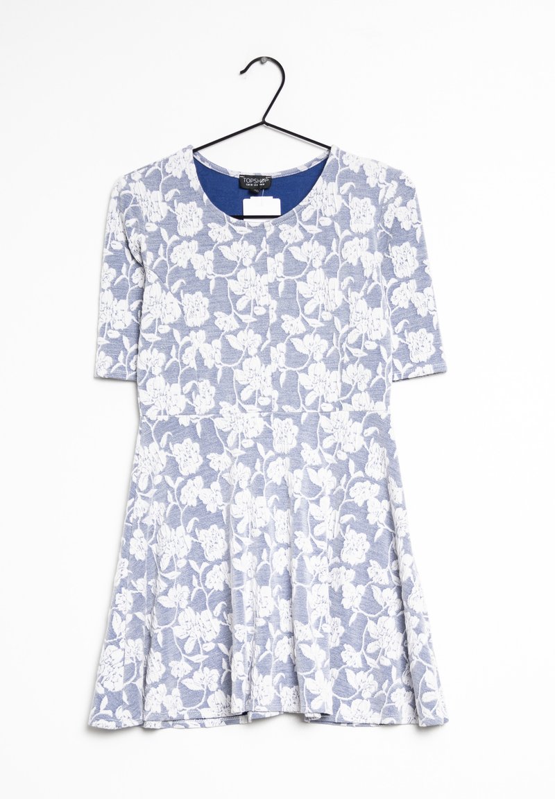 Blåblommig klänning med korta ärmar, med ett vitt blommönster, rund halsringning och utsvängd kjol. Hänger från en svart krok.