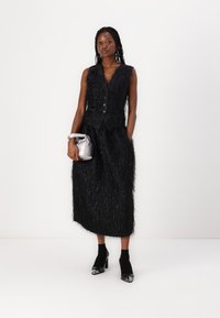 Black textured dress with a fitted bodice, v-neck, and button details, paired with a silver pouch and black heeled ankle boots.
