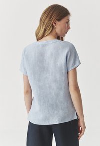 Top in lino azzurro chiaro con maniche corte, scollatura rotonda e un aspetto leggermente texturizzato. La vista posteriore mostra una vestibilità rilassata e un design casual.