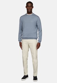 Light blue knit sweater with ribbed cuffs, paired with cream-colored tailored pants and black sneakers; simple and contemporary design.