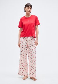 T-shirt rouge en coton à manches courtes associée à un pantalon blanc avec un motif cerise. Coupe ample avec des jambes décontractées, design à la fois casual et harmonieux.