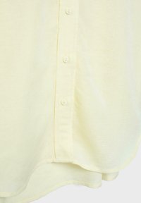 Jasnożółta koszula na guziki ukazująca teksturę tkaniny oraz dolną część z zaokrąglonym brzegiem.