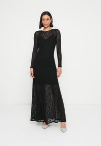 Črna maxi obleka iz čipke z dolgimi rokavi, oprijetim korzetnim delom in prosojnim spodnjim delom. Ima zaobljen izrez in teksturirano tkanino.