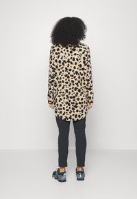 Dlouhý rukáv, béžový fleecový top s černými leopardími skvrnami a logem na zádech, spárovaný s černými kalhotami a multibarevnými teniskami.