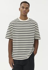 Dryžuotas marškinėlis kreminės ir juodos spalvos iš medvilnės; trumpomis rankovėmis, apvalia kaklo iškirpte, su horizontaliais dryžiais ir laisvu siluetu.