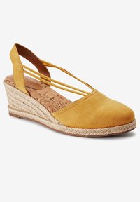 Espadrille compensée en suède jaune avec un design à lanières et une semelle en jute tissée. Dotée d'un bout arrondi et d'une semelle intérieure en liège naturel.