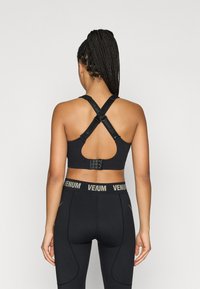 Melnā sporta krūšturis ar krustveida lencēm un atvērtu muguru. Ir regulējami āķi un logotipa detaļas. Kombinēts ar melnām sporta legingām.