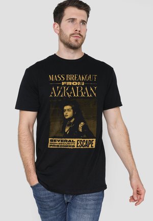 Mann trägt schwarzes T-Shirt mit goldener Schrift "Mass Breakout from Azkaban" und Bild einer Frau mit Text "Several High-Security Prisoners Escape."