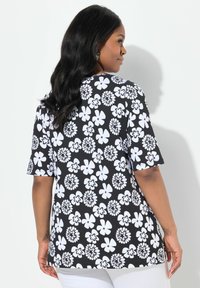 Top negro con un estampado floral blanco en toda su superficie, mangas cortas y un dobladillo redondeado. El material parece suave y ligero.