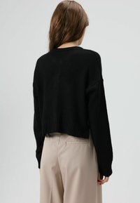 Zwart, cropped gebreide trui met geribbelde zoom en manchetten. Gecombineerd met lichtbeige, hooggesneden broek, gladde textuur, zonder zichtbare patronen.