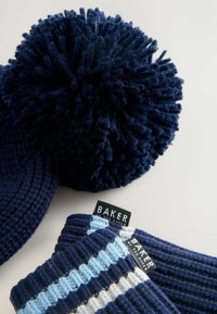 Een navyblauwe gebreide muts met een grote pompon en bijpassende vingervrije handschoenen met horizontale blauwe strepen en een 'BAKER'-label.