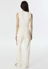 Witte mouwloze top met een geribbelde textuur; gecombineerd met off-white, loszittende broeken met subtiele borduurdetails op het been.