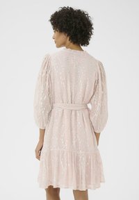 Vestido rosa claro con mangas abullonadas, cintura ceñida y dobladillo en capas. Presenta patrones en forma de lentejuelas plateadas por todo el tejido.