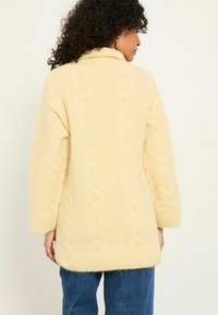 Gelber Strickpullover mit umgeschlagenem Kragen, langen Ärmeln und lockerer Passform. Weiche Textur mit geripptem Saum und Ärmeln.