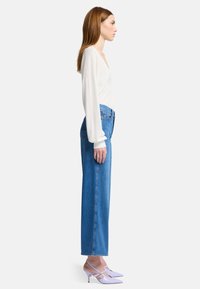 Top bianco a maniche lunghe, jeans blu a gamba dritta e décolleté punta acuminata lavanda. Caratteristiche notevoli: vestibilità comoda e trama di tessuto leggera.