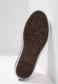 Brązowa guma podeszwy sportowej obuwia z wyraźnym wzorem antypoślizgowym, biała śródpodeszwa i czarny pasek na krawędzi z logo "Converse All Star".