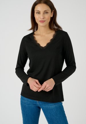 Zwarte langslaper top met een V-hals en kantafwerking. De stof is zacht en heeft een gladde textuur. Gecombineerd met blauwe jeans.