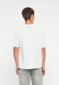 Hvit bomulls t-skjorte med rund hals og korte ermer. Baksiden har en liten etikett ved halsen. Enkel, klassisk design.