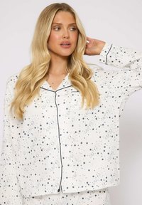 Haut de pyjama blanc avec un motif d'étoiles navy, devant boutonné, poche poitrine, col à revers et manches longues avec des accents de passepoil foncé.