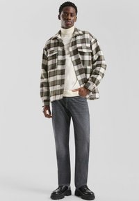 Geruit flanellen overhemd in groen en wit, gedragen over een crèmekleurige coltrui. Gecombineerd met grijze spijkerbroek en zwarte stevige schoenen.