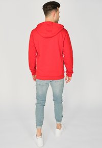 Rød hættetrøje med en rummelig hætte, lange ærmer og ribbind. Bæres med lyseblå skinny jeans og hvide sneakers.