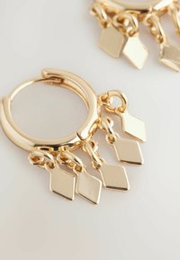 Orecchini a cerchio in oro con tre pendenti a forma di diamante, caratterizzati da una finitura lucida e catene collegate per un movimento elegante.