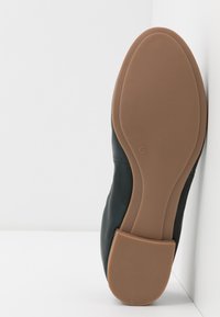 Chaussure en cuir noir avec une semelle en caoutchouc flexible. La semelle a une finition lisse, de couleur beige, avec un motif texturé distinct. Taille indiquée comme 37.