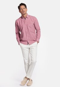 Rood-wit geblokte blouse met lange mouwen en een voorzak, gecombineerd met witte broek en beige instappers.
