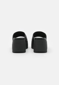 Sandalias de plataforma negras con una correa ancha, forma redondeada y parte superior texturizada. Presentan tacones gruesos y sólidos, con un diseño minimalista.