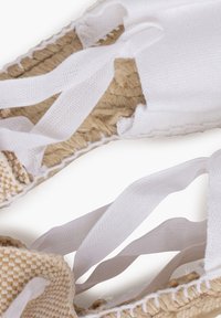 Espadrillas bianche in tela con suola in juta intrecciata. Presentano lacci bianchi che si incrociano su una parte superiore in tessuto testurizzato.