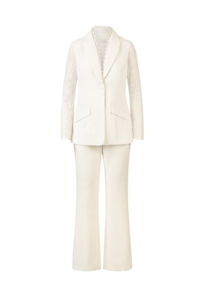Weißer Anzug, der aus einem maßgeschneiderten Blazer mit langen Spitzenärmeln und einer kremfarbenen, ausgestellten Hose mit Taschen besteht.
