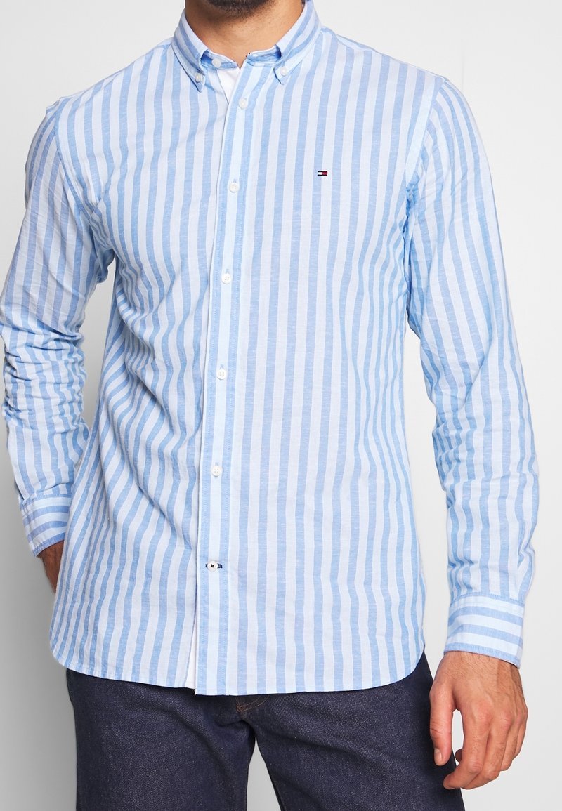 Light blue striped shirt made of cotton. Features a button-down collar, long sleeves, and small logo on the chest. Tailored fit.