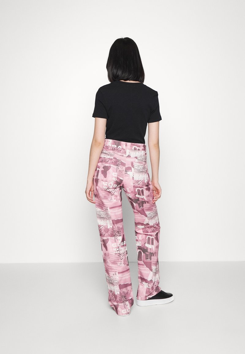 Pantalons roses à motifs avec un design en collage et des éléments textuels, associés à un haut à manches courtes noir. Tissu lisse, coupe évasée.
