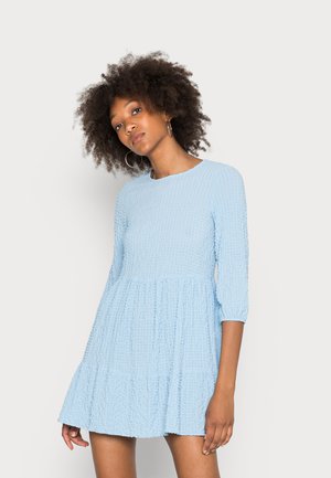 Vestido texturizado azul claro com mangas de três quartos e saia em camadas. Apresenta um decote redondo e detalhes franzidos por todo o tecido.