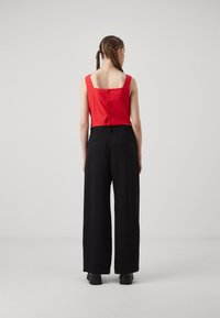 Red linen cropped top with square back and button closure, paired with high-waisted black wide-leg trousers, view from the back.