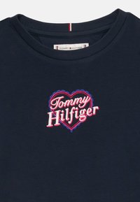 Μπλε σκούρο μπλουζάκι με στρογγυλή λαιμόκοψη, με κεντημένη κόκκινη και μπλε καρδιά και κείμενο "Tommy Hilfiger" στο στήθος.