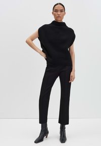 Pull col roulé noir à côtes avec des manches larges, associé à un pantalon noir chic et des bottines à bout pointu. Texture lisse, silhouette ajustée.