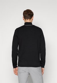 Black long-sleeve polo shirt with a high collar, featuring white piping along the collar and textured detailing on the shoulders.