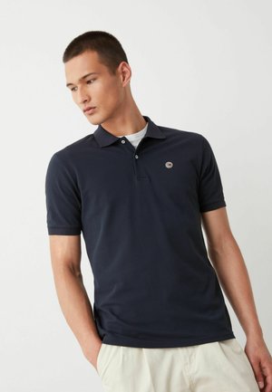 Marineblauwe polo gemaakt van lichtgewicht katoen, met een klassieke kraag, korte mouwen en een klein rond logo op de borst.