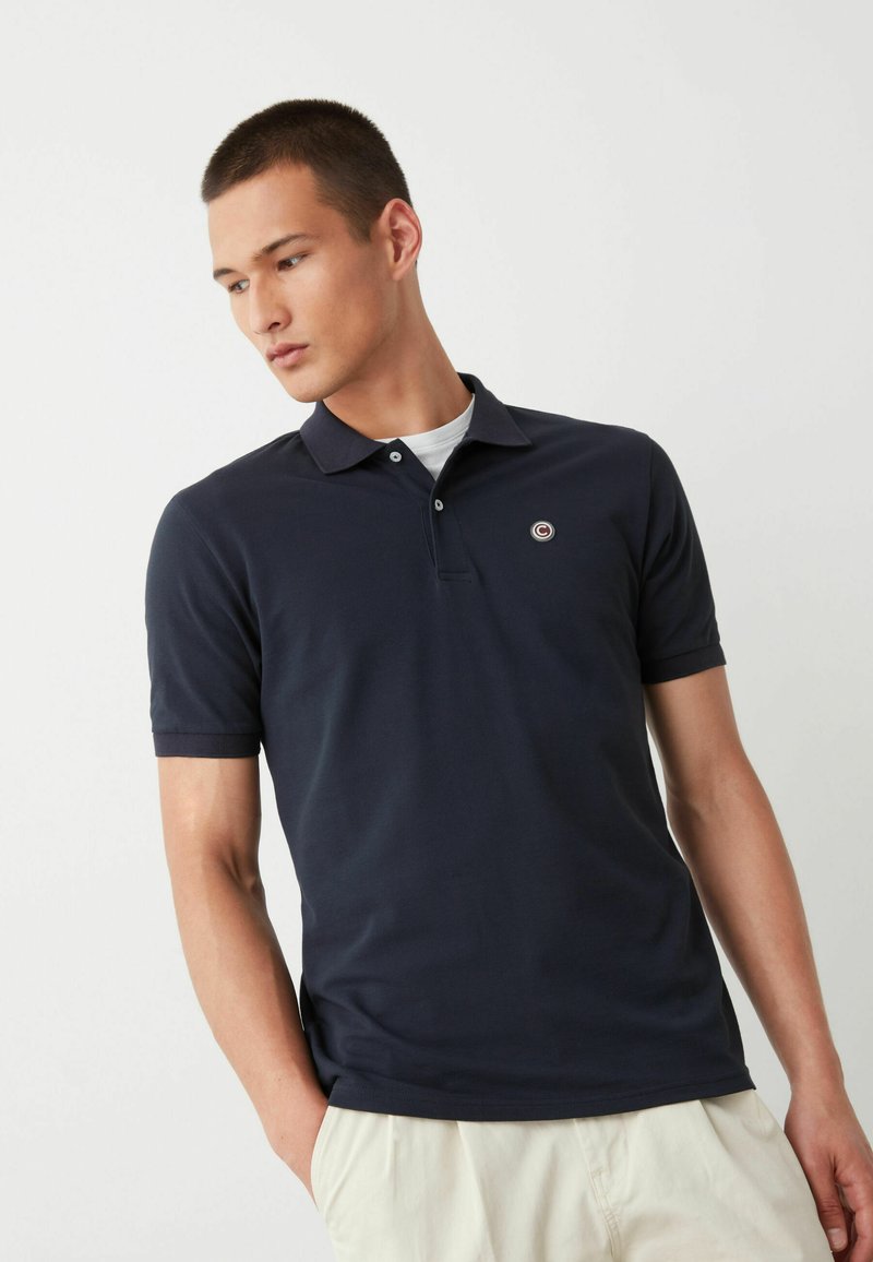 Tumed polo-särk, mis on valmistatud kergest puuvillast, klassikalise krae, lühikeste varrukate ja väikese ümmarguse logoga rinnal.