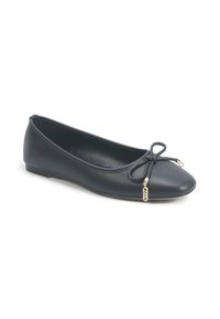 Ballerines en cuir noir avec bout rond, détail de nœud à l'avant et petites accents en charme doré sur fond blanc.
