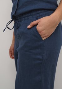 Mornarji modre lanene hlače z elastičnim pasom in nastavljivo vezalko, ki imajo bočne žepke in gladko teksturo.