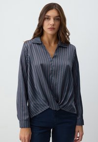 Camicia a maniche lunghe blu navy a righe con colletto e dettaglio annodato sul davanti. Il materiale è liscio con una leggera lucentezza.