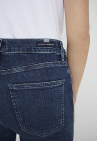 Mörkblå denimjeans med bakficka och "CITIZENS of HUMANITY"-märke på midjebandet. Slät textur, rak passform.