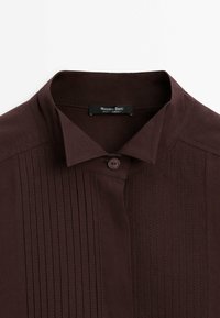 Chemise marron foncé avec un col mandarin, fermeture à boutons et des rayures verticales. L'étiquette indique "Massimo Dutti, fabriqué en Turquie."