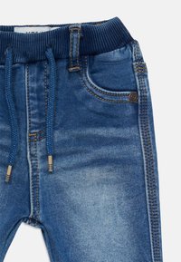 Pantalones jogger de denim azul con cinturilla elástica acanalada, cordón ajustable, bolsillos frontales y detalles de lavado deslavado.