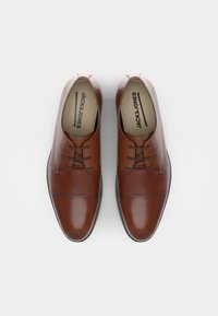 Chaussures habillées en cuir marron avec une finition lisse, bout arrondi, design à lacets et accents texturés sur la tige. Nom de la marque visible à l'intérieur.