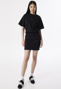 Czarna, krótko rękawowa, dopasowana sukienka z elastyczną talią. Gładki materiał, minimalistyczny design, z małym akcentem logo z przodu. Połączona z czarnymi trampkami.