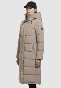 Beige lange pufferjas met een hoge kraag, oversized capuchon, twee zijzakken en een logo-accent op de mouw. Glad textuur, ritsluiting.