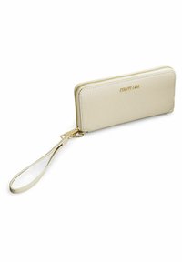 Portefeuille en cuir crème avec finition texturée, fermeture zippée et cordon de poignet. Présente des éléments en métal doré et un logo de marque en relief à l'avant.